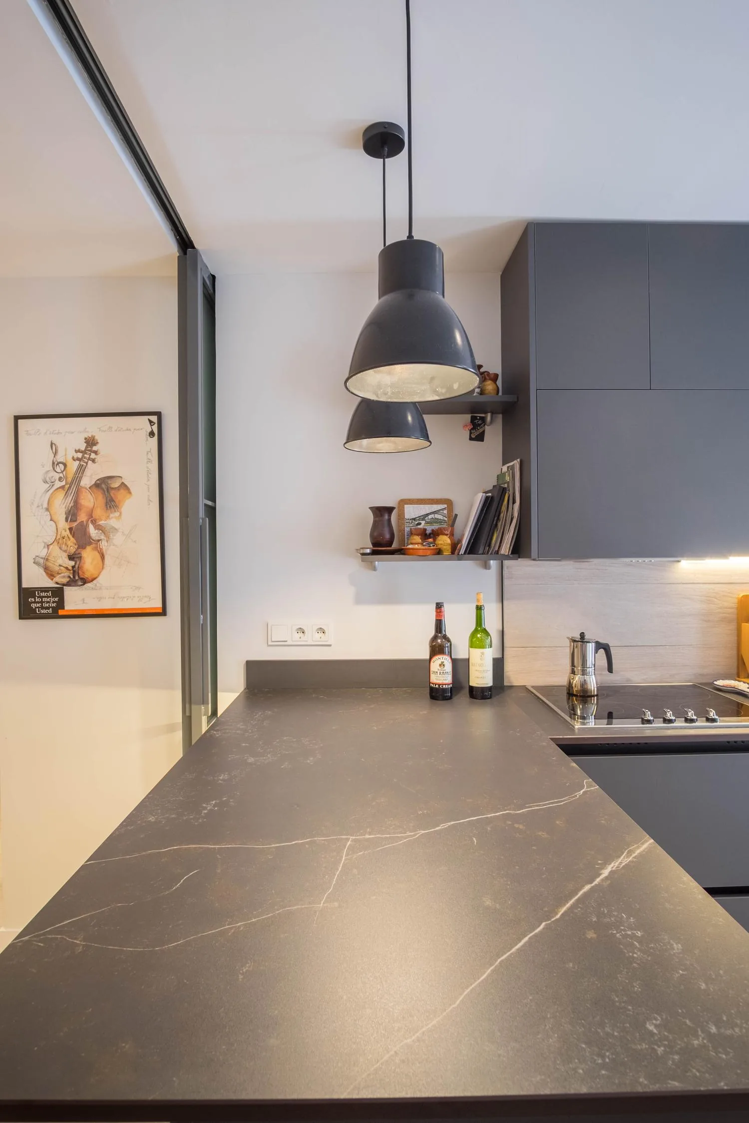 Detalle de la encimera de piedra oscura de la cocina, bajo lámparas colgantes