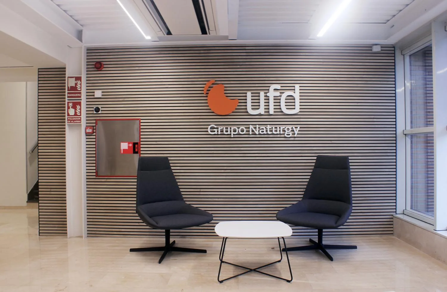 Zona de acceso y recepción de UFD Naturgy, con asientos de espera y luz natura Zona de acceso y recepción de UFD Naturgy, con asientos de espera y luz natura