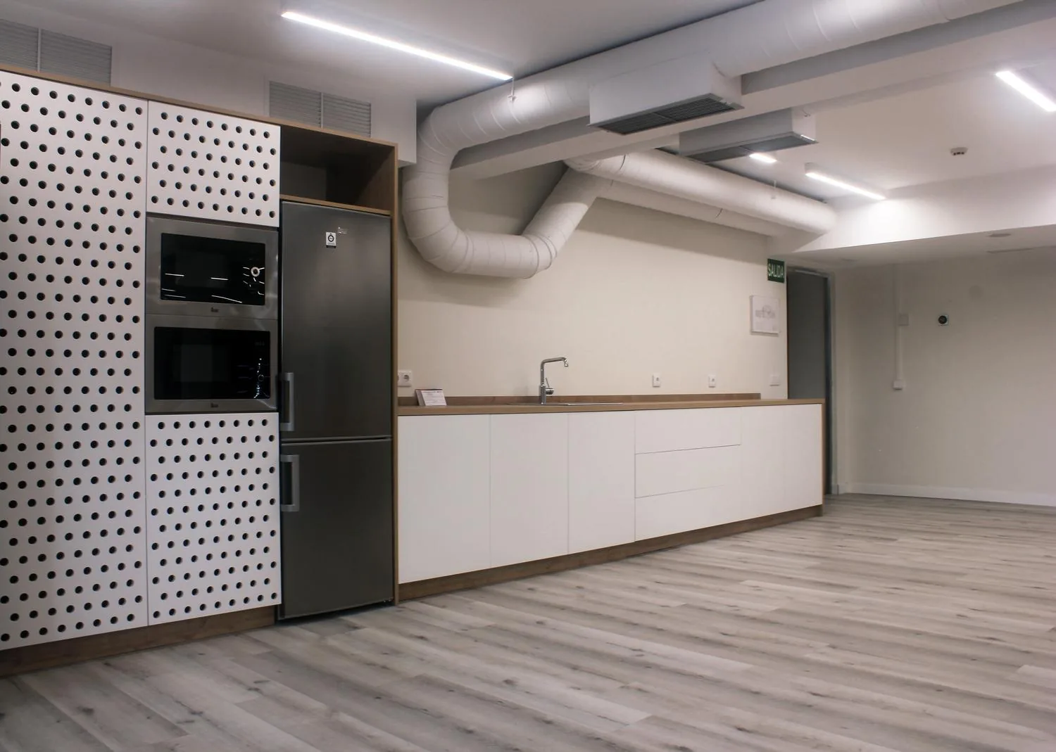 Zona de office y cocina de la oficina de UFD Naturgy, con panel perforado y electrodomésticos